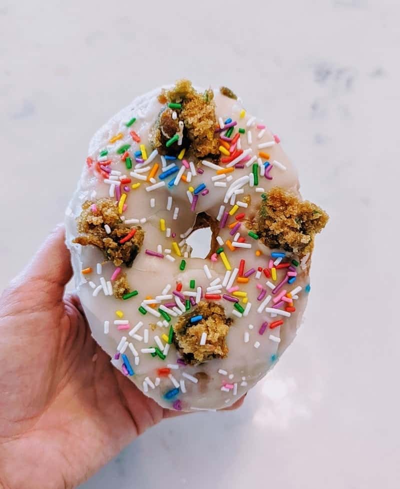a single vegan donut covered in white icing and topped with colorful sprinkles and chunks of cookie dough in toronto
