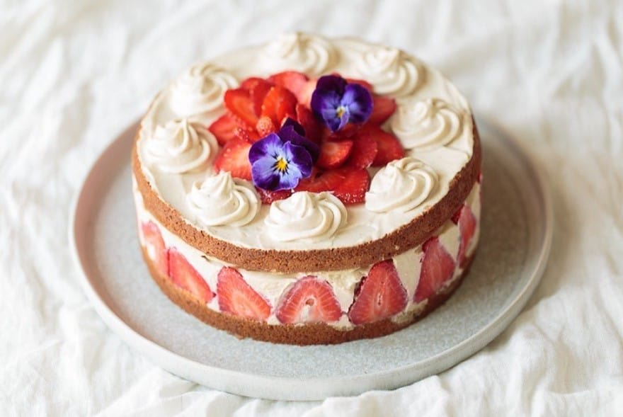 vegan and gluten free cake with a layer of cream and sliced strawberries in the middle and topped with more cream and edible flowers in vienna