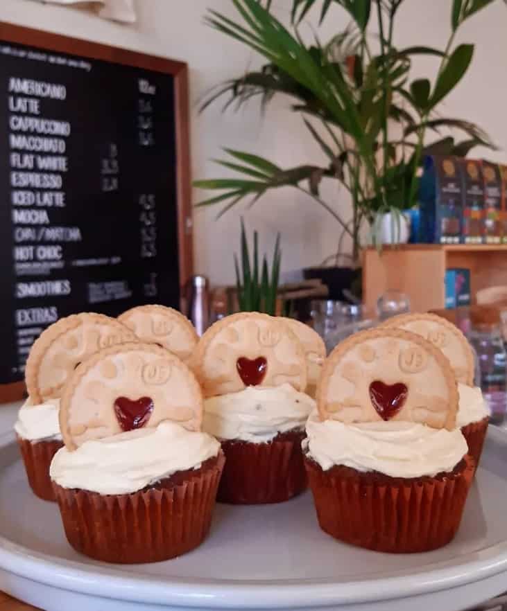 six vegan cupcakes topped with vanilla buttercream and jammy dodger cookies on top sitting on a coffee house counter in edinburgh