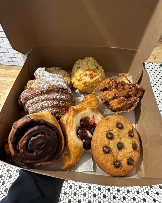 a cardboard box filled with six vegan pastries like cookies, croissants, and a danish from clementine vegan bakery in brooklyn