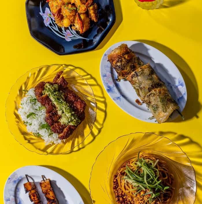 a large spread of small vegan chinese dishes spread across a bright yellow table at facing heaven in london