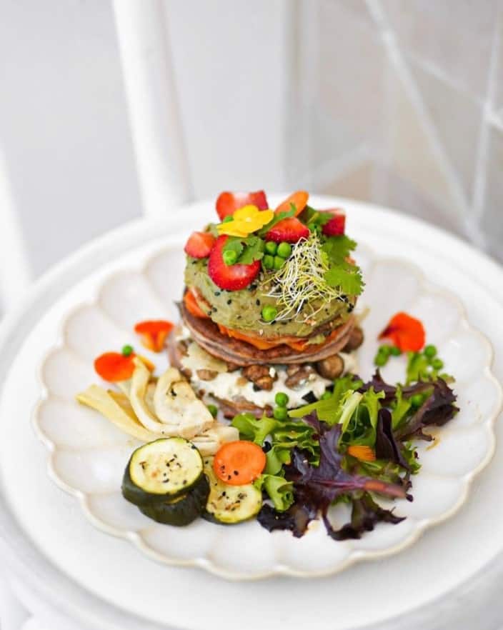 a small stack of savory pancakes topped with avocado and roasted vegetables on a white plate at ground to grow at brunch in paris