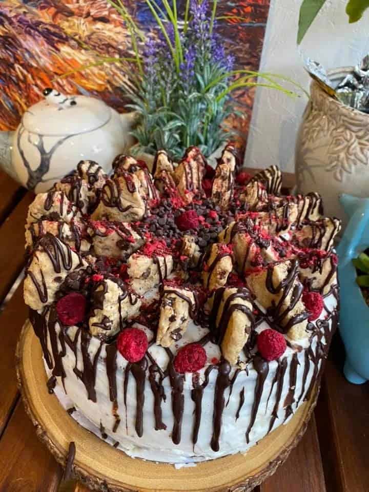 vegan cake covered in a white buttercream and topped with chunks of cookies and slices of strawberries and then heavily drizzled with chocolate at happy zoe vegan bakery in brooklyn