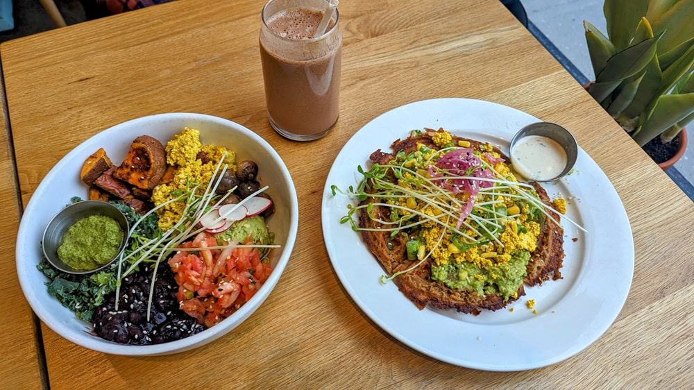 savory vegan waffle topped with tofu scramble next to a breakfast bowl on a wood table at kupert and kim in toronto