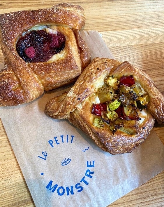 two golden vegan pastries on a wax sleeve with the logo for le petit monstre in brooklyn