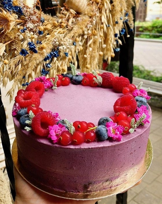 a beautiful purple vegan cake topped with a ring of fresh fruit sitting in a window in budapest