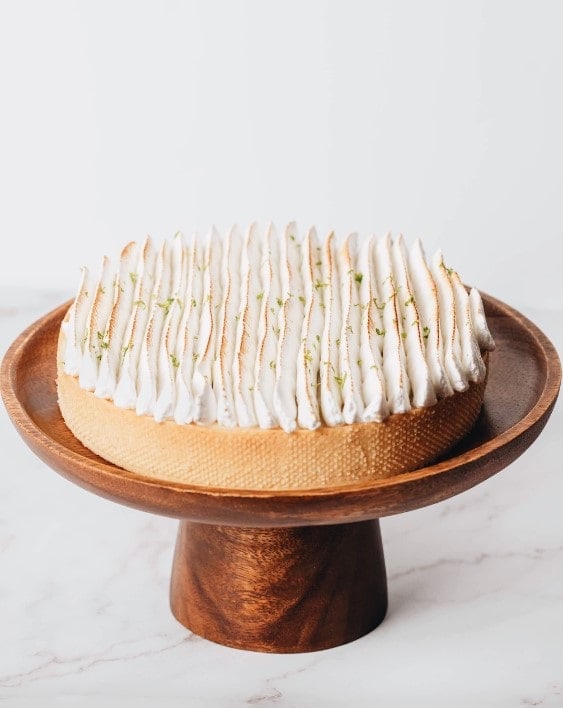 a round vegan key lime pie topped with a lightly golden meringue, sitting on a bronze cake stand in barcelona 