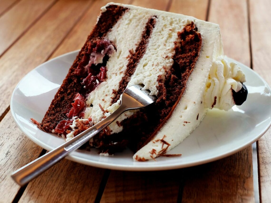 a large slice of vegan red velvet cake with white cream frosting on a white plate at a bakery in budapest