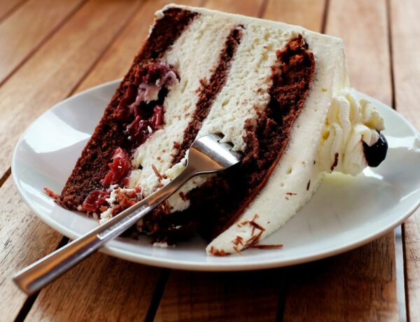 a large slice of vegan red velvet cake with white cream frosting on a white plate at a bakery in budapest