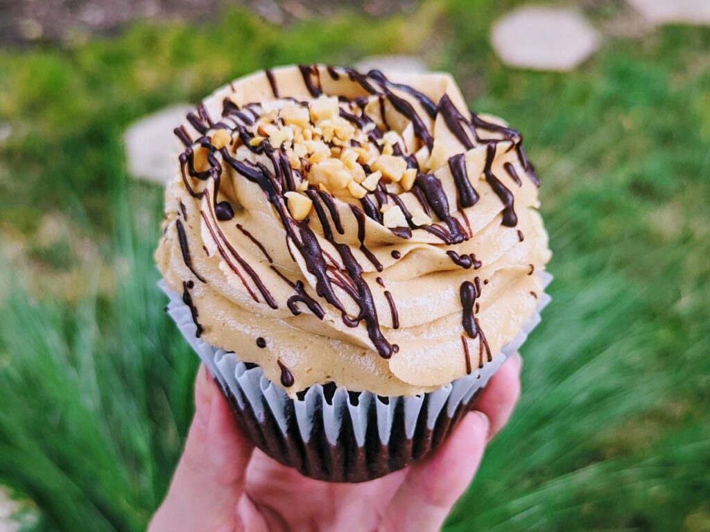 vegan chocolate cupcake topped with a peanut butter butter cream swirl and topped with a drizzle of chocolate and chopped peanuts