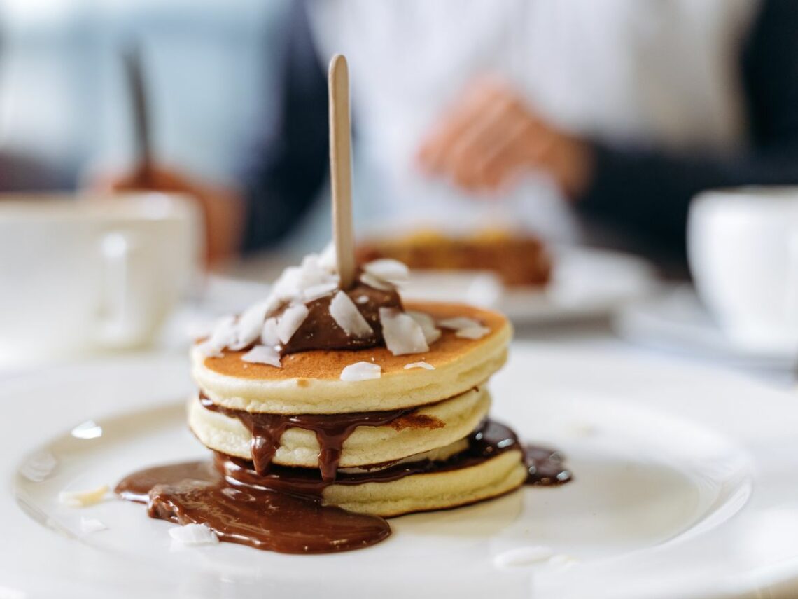 a small stack of three mini golden vegan pancakes covered in chocolate sauce with a wood stick in the middle in paris