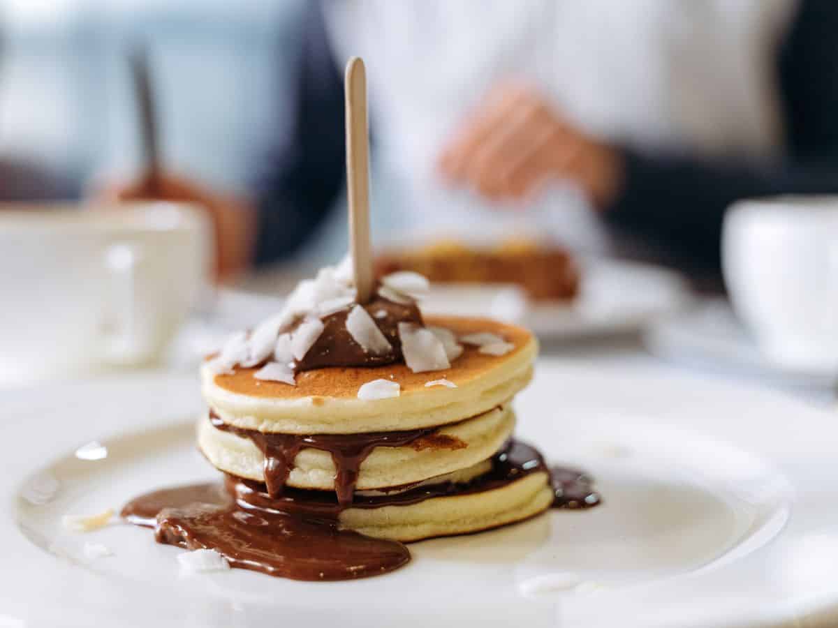 a small stack of three mini golden vegan pancakes covered in chocolate sauce with a wood stick in the middle in paris