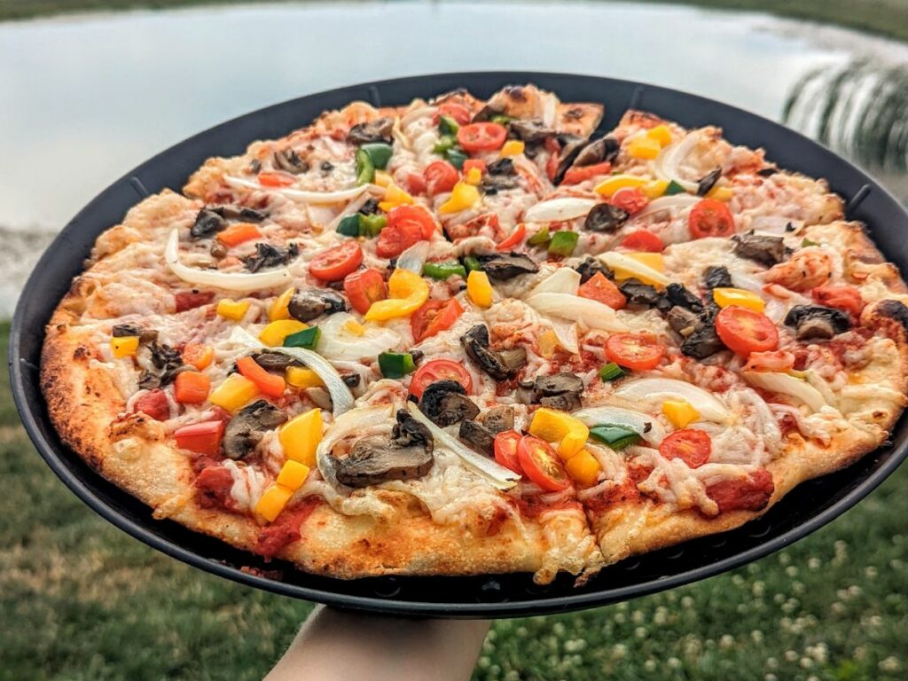 round vegan pizza held with one hand in front of a lake in the finger lakes