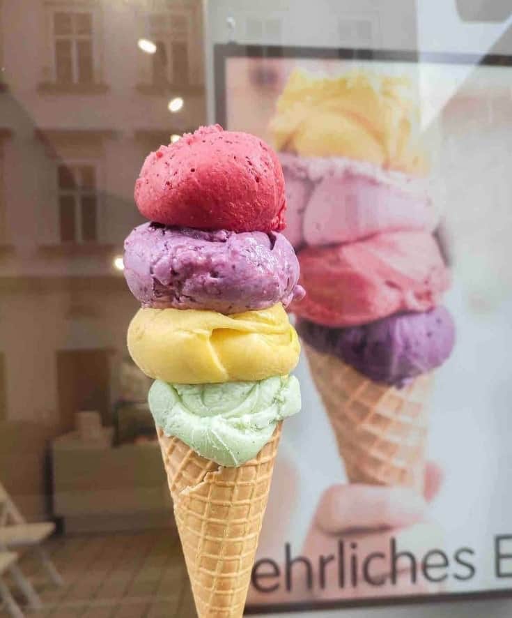 a small vegan ice cream cone topped with four scoops of colorful vegan ice cream scoops in raspberry, blueberry, lemon, and pistachio in vienna