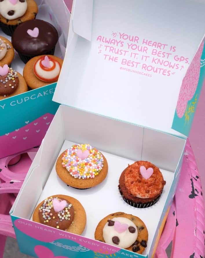 a pink and blue box with four colorful vegan cupcakes inside from the vegan bakery bunnie cakes in miami