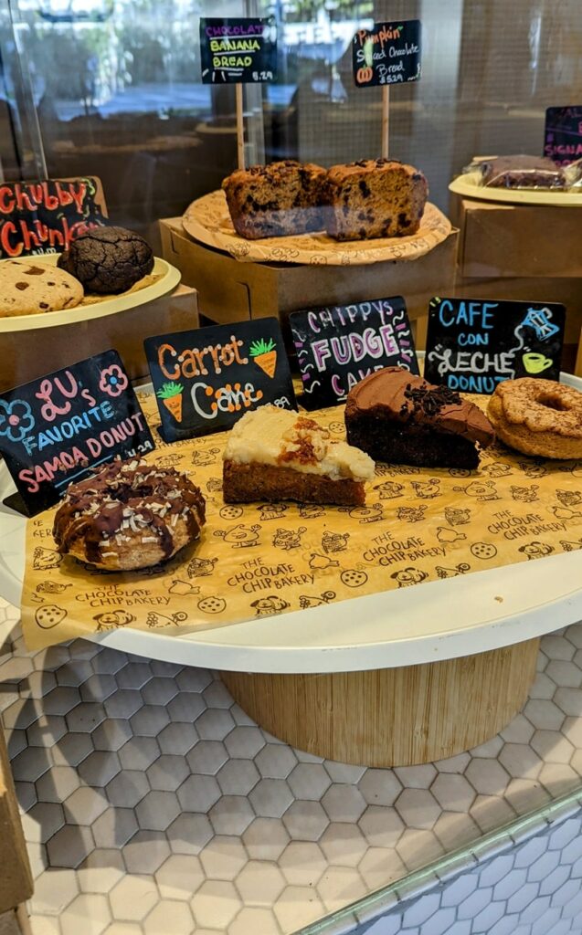 a display of vegan cakes, sweet bread, donuts, and more inside of a dessert case at the chocolate chip vegan bakery in miami
