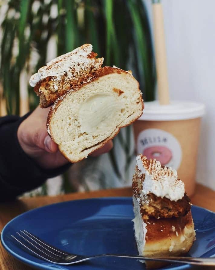 a vegan tiramisu donut cut in half exposing the coffee cream in the middle next to a coffee at a vegan bakery in madrid