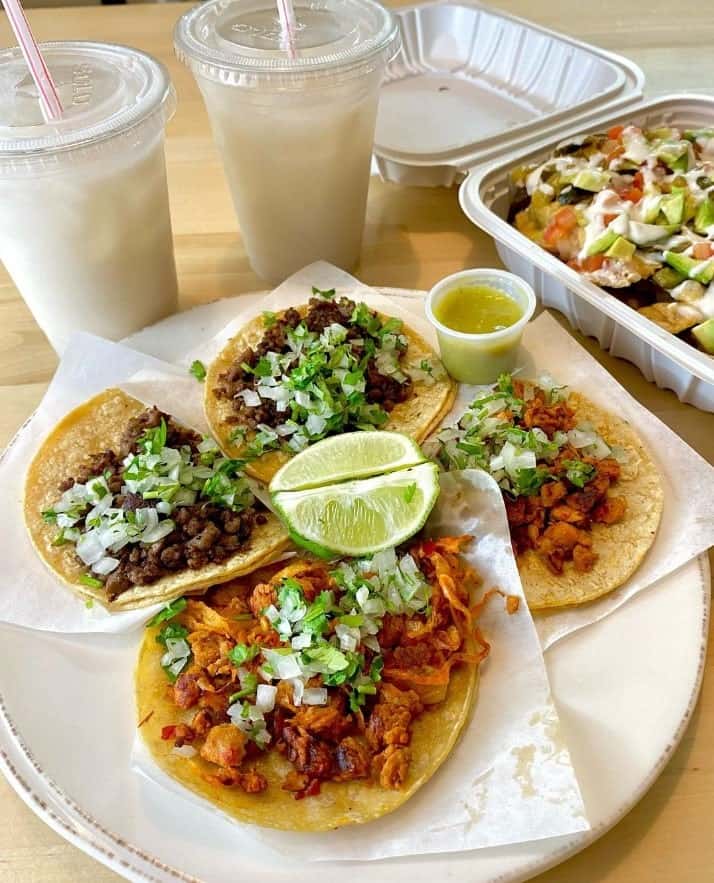 a plate with four vegan tacos next to a take out box with nachos and two horchata drinks at healthy substance in chicago