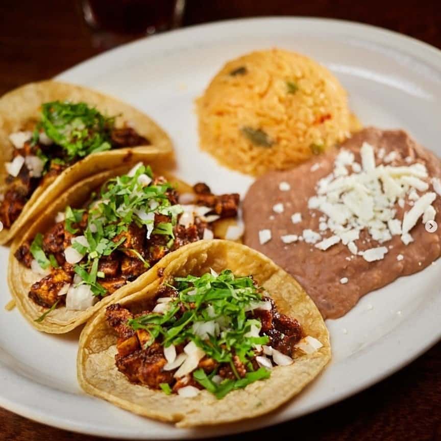 a round plate with three vegan meat tacos next to refried beans and rice at la cantina in chicago