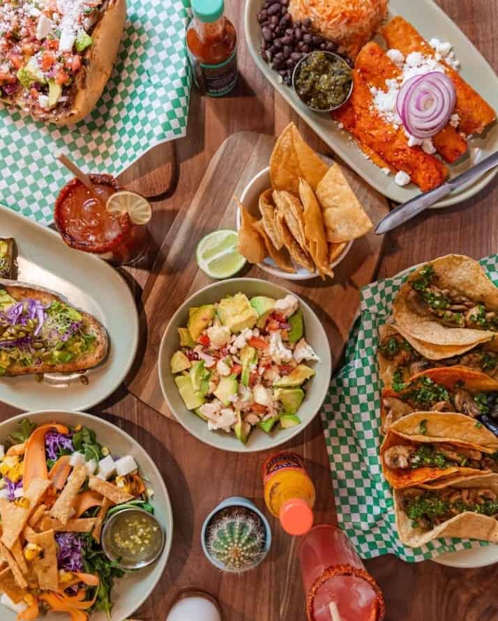a large spread of vegan mexican food across a wood table with tacos, guacamole, torta, and more at penelopes vegan taaqueria in chicago