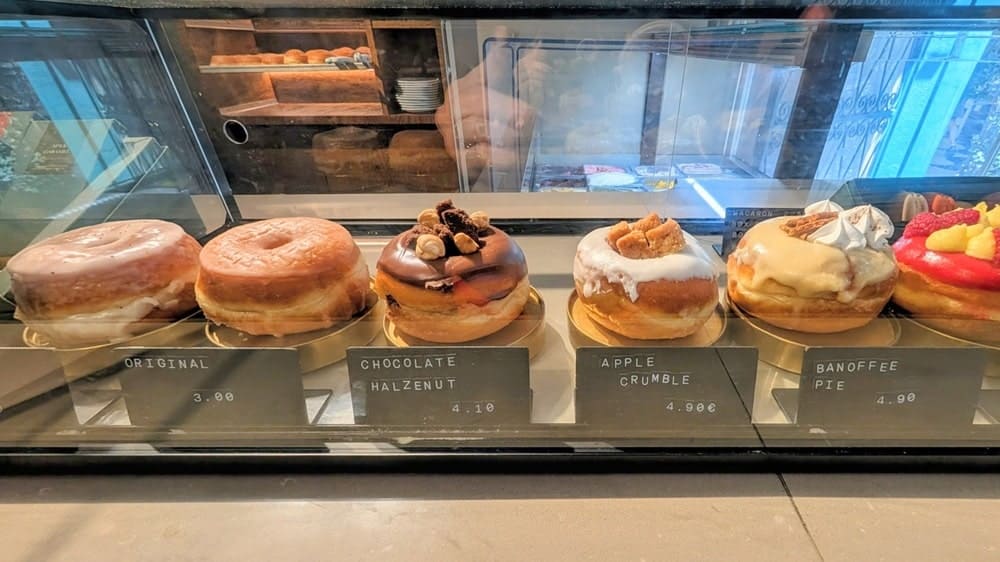 a dessert case filled with six different vegan donuts at scoop n dough in lisbon