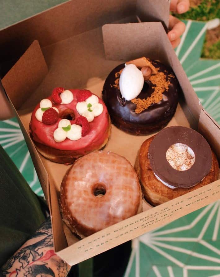 a brown box with four vegan donuts topped with pink icing, dark chocolate and sugar glaze in lisbon