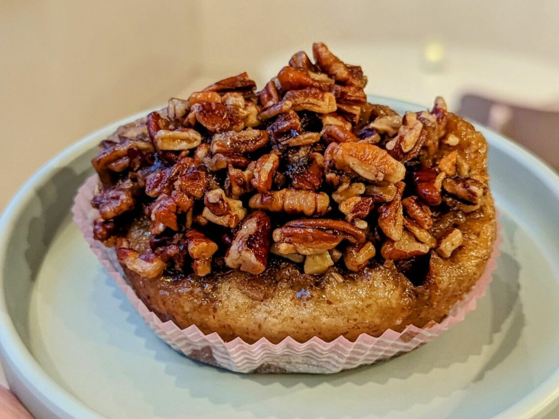 a large golden vegan cinnamon bun topped with chopped pecans on a teal plate at a vegan bakery