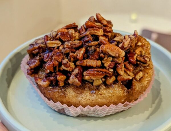 a large golden vegan cinnamon bun topped with chopped pecans on a teal plate at a vegan bakery