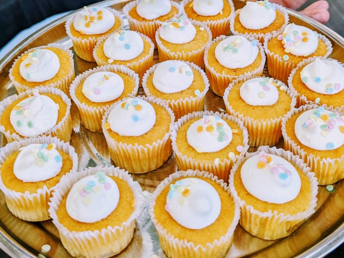 a tray of mini vegan vanilla cupcakes topped with small swirls of white frosting with colorful sprinkles at a vegan bakery in lisbon