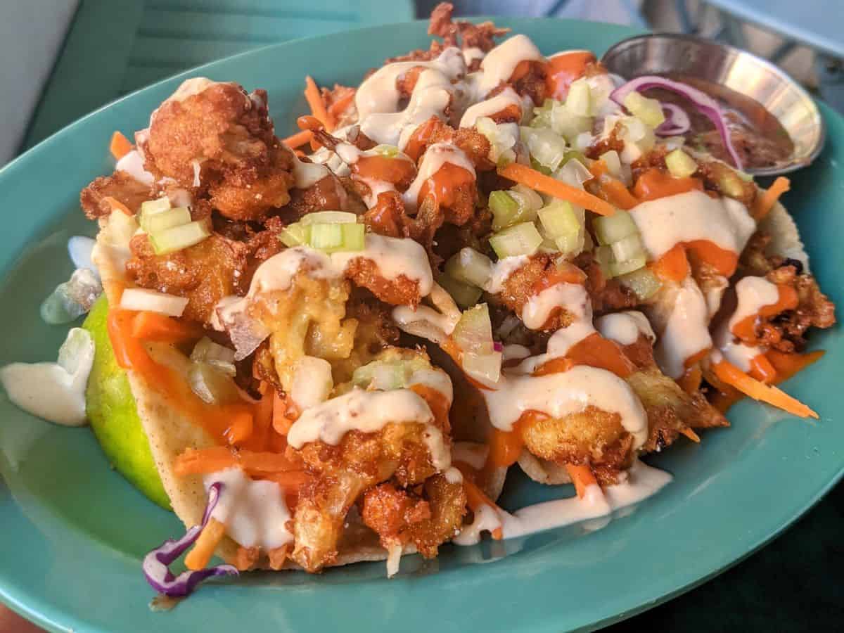 vegan mexican food consisting of a teal plate with two giant buffalo cauliflower tacos covered in hot sauce and a cashew cream