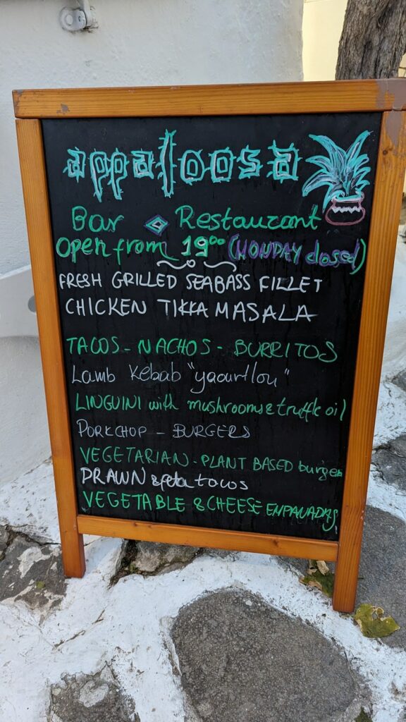 a chalk board sign highlighting menu specials outside of the vegan-friendly restaurant appaloosa in mykonos 