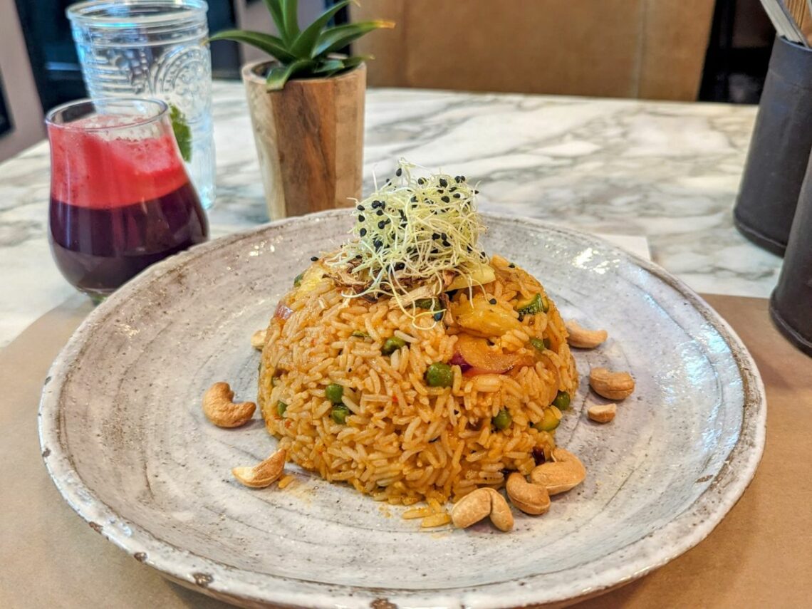 a large mound of vegan fried rice with pineapple, tempeh, and cashews next to a pink beet juice at the vegan restaurant winners in athens greece