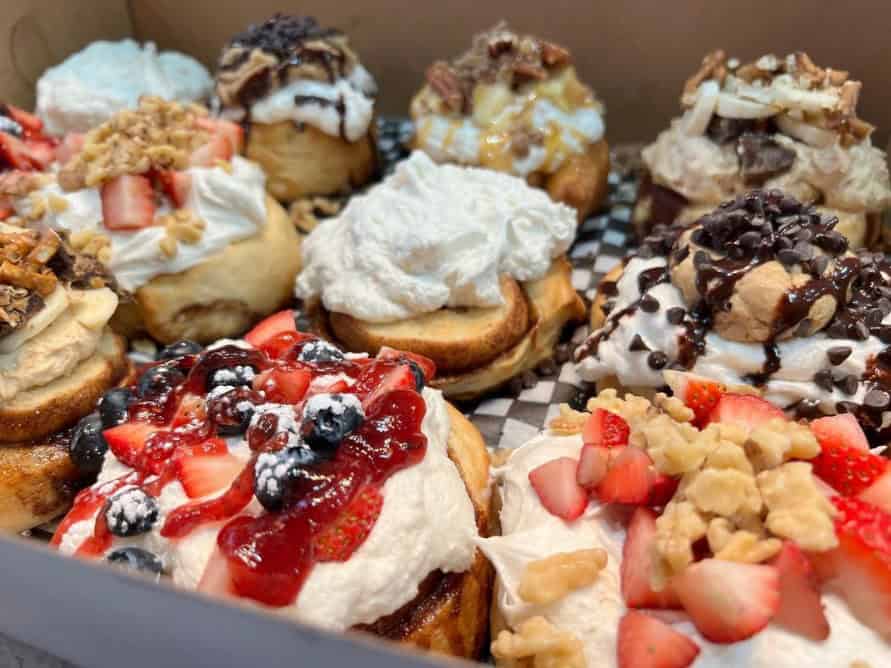 a box of six vegan cinnamon rolls topped with frosting, cookie dough, chocolate, berries and more from cinnaholic