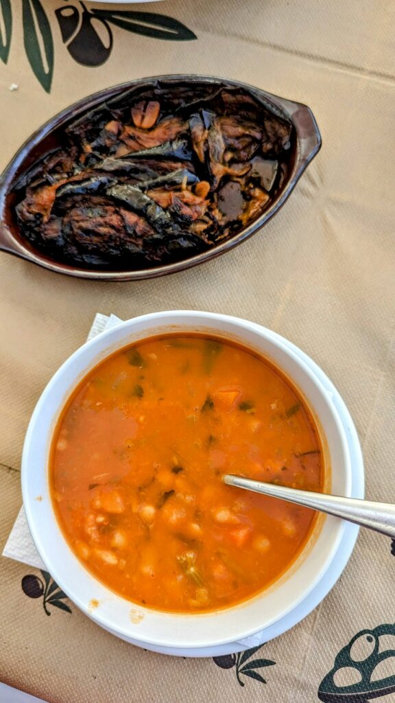 a large bowl of bright orange white bean soup next to a small dish with roasted eggplant