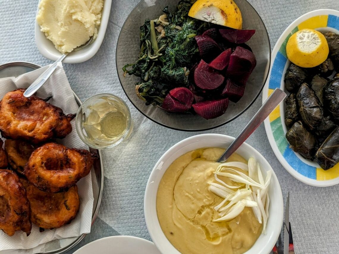 a spread of vegan greek dishes like fava, beets, grape leaves, and tomato fritters on a table