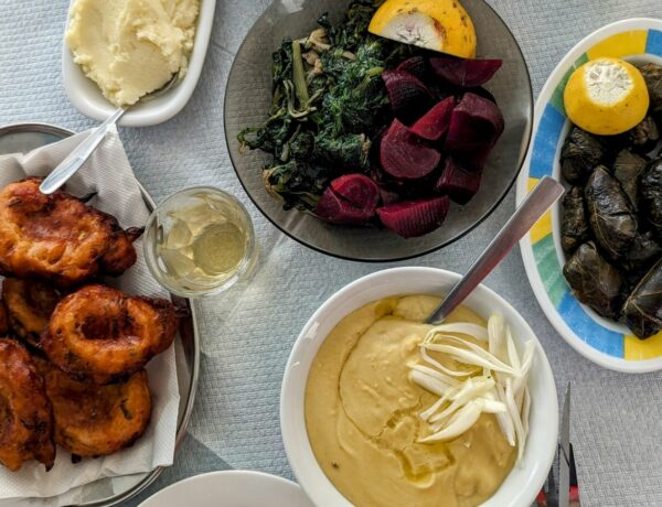 a spread of vegan greek dishes like fava, beets, grape leaves, and tomato fritters on a table