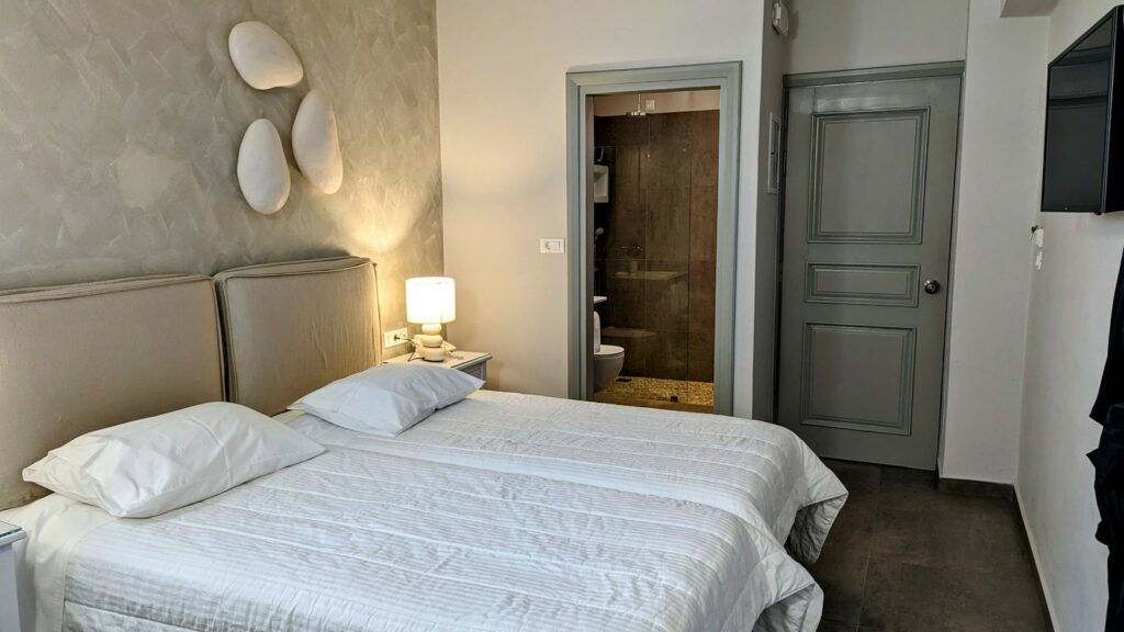 double guest bedroom with light colored walls and bedding at the vegan friendly hotel grotta in naxos