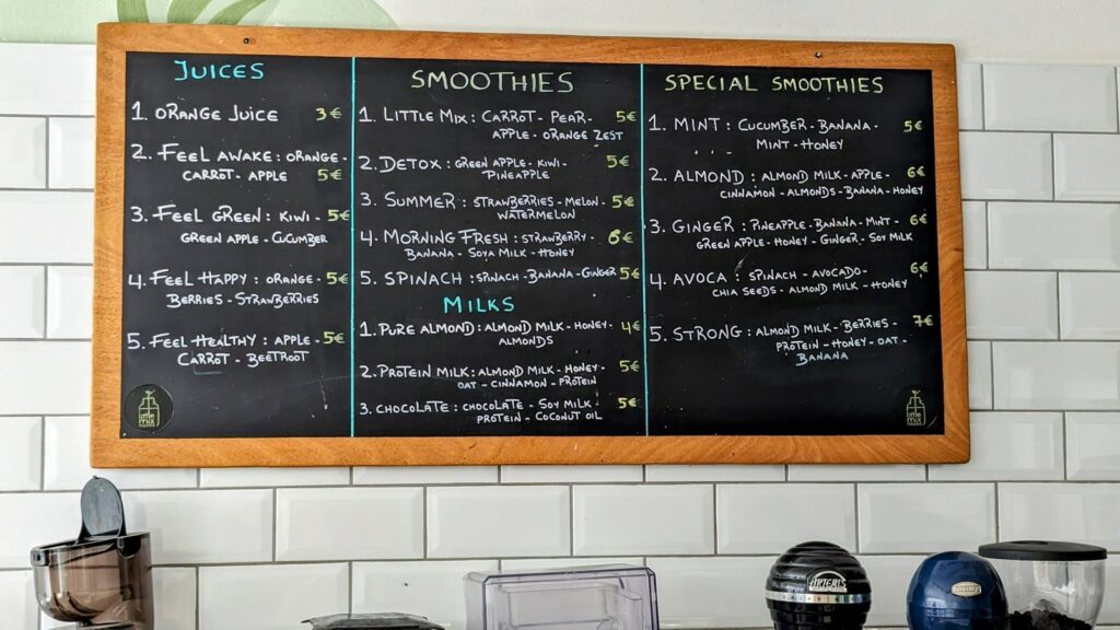 a chalk board sign listing all of the smoothies and juices available at juicy girl in naxos
