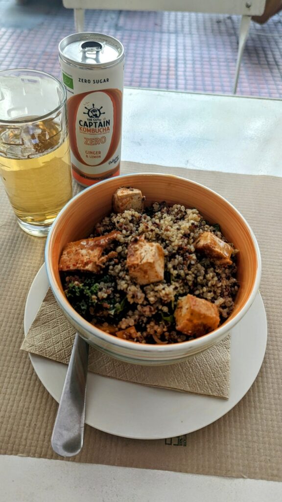 a small macrobiotic vegan salad with quinoa, tofu chunks and kale, next to a can of kombucha at mama tierra in athens