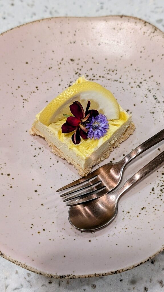 a small square vegan lemon cheese cake topped with a purple flower in bangkok