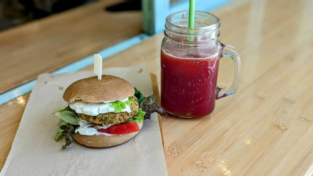 a vegan burger with lettuce, tomato, and mayo on a paper tray next to a purple beet juice at the cafe peas vegan and raw food in athens