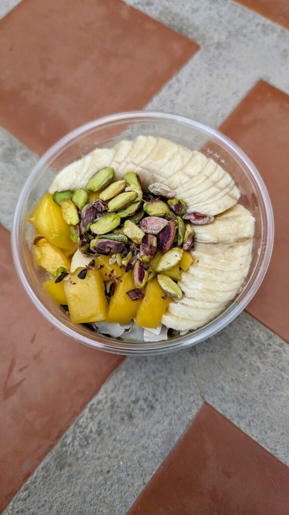a small round green smoothie bowl topped with sliced bananas, mango and chopped nuts from stolen fruit in santorini