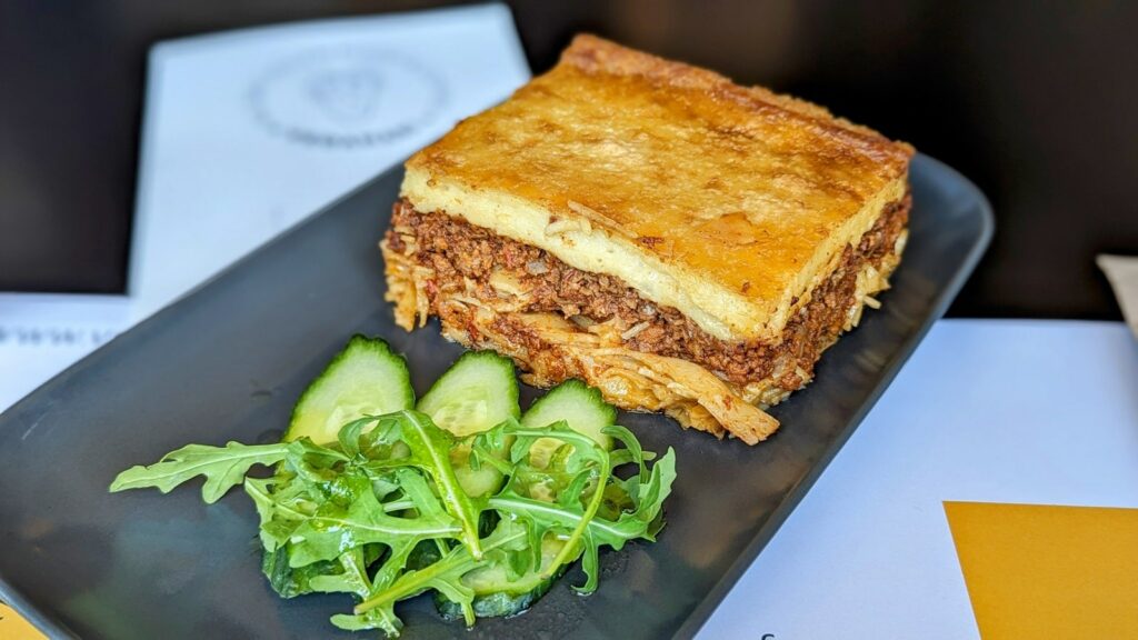 a giant slice of greek vegan pastitsio on a black plate with a green garnish 