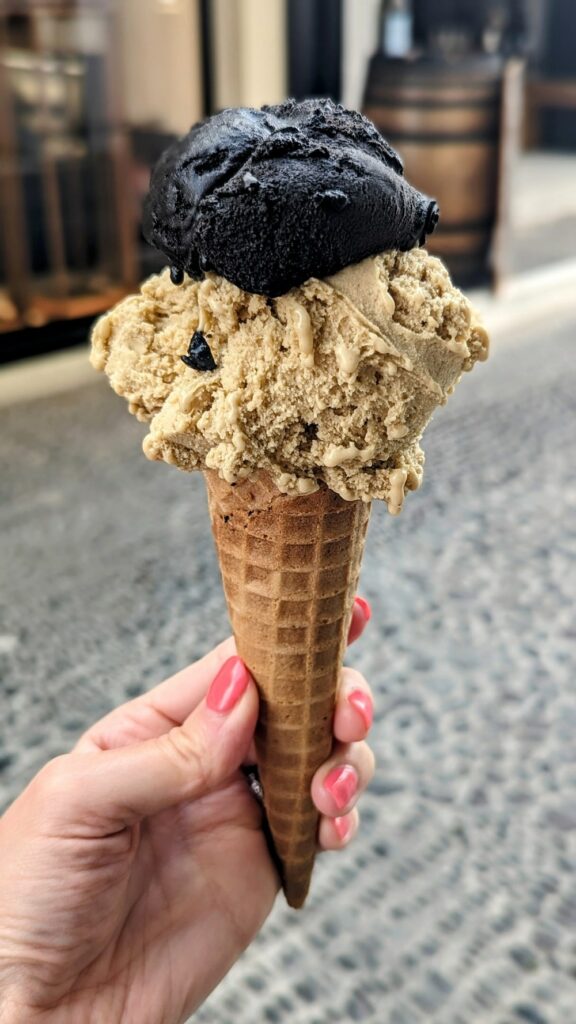 two scoops of vegan ice cream on a golden cone held in an empty street in santorini from zotos