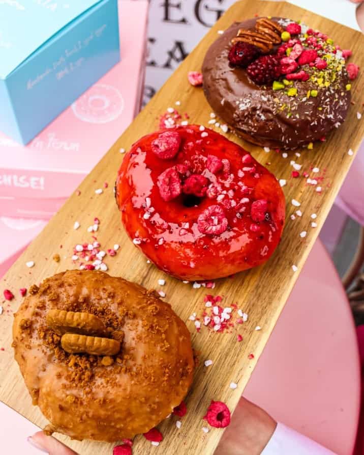 a long rectangle tray with three bright vegan donuts topped with icing, chocolate and nuts at La Donuteria Praha