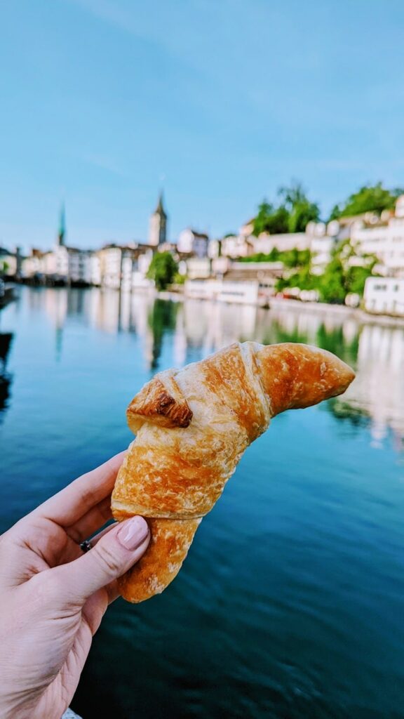 a single vegan croissant held in front of a river in zurich