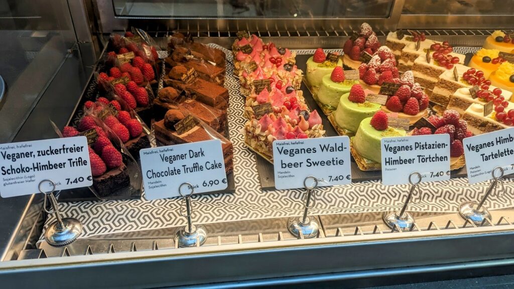 rows of colorful vegan pastries in a dessert case with signs in front of them in hamburg