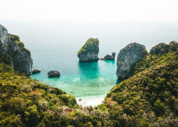 lush green jungle surrounding a white sand beach and turquoise water in thailand
