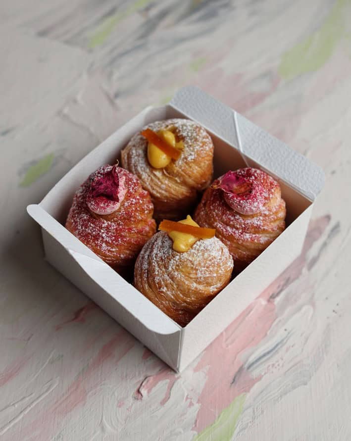 a white box with four golden vegan krafin pastries topped with sugar, cream, and fruit in prague