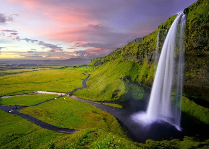the famous seljalandsfoss waterfall with a purple and pink sunset in the background in iceland